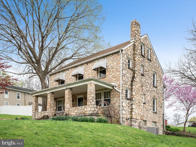 view of front of home with a front lawn, fence, stone siding, and a chimney