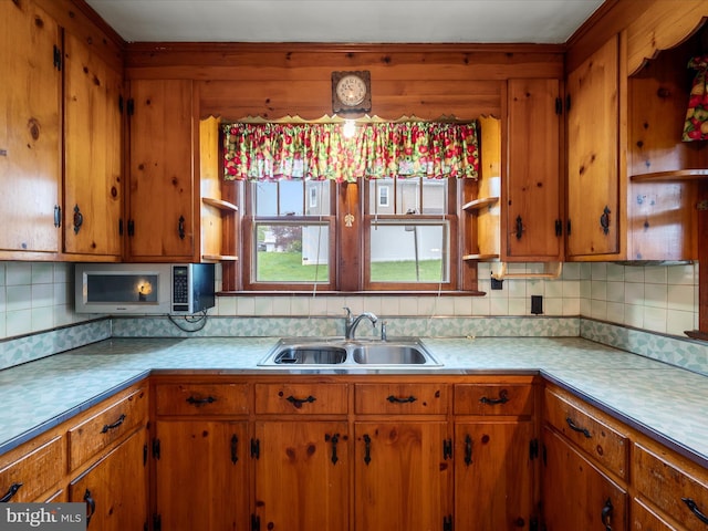 kitchen featuring open shelves, stainless steel microwave, light countertops, a sink, and backsplash