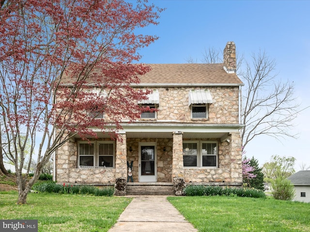 view of front of property with roof with shingles, stone siding, a chimney, and a front lawn