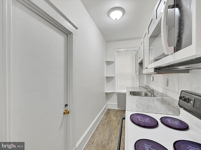 kitchen with baseboards, white appliances, light countertops, light wood finished floors, and a sink