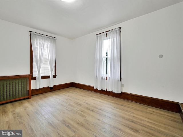 unfurnished room with baseboards, radiator, and wood finished floors