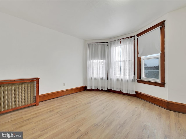 unfurnished room with radiator, wood finished floors, and baseboards