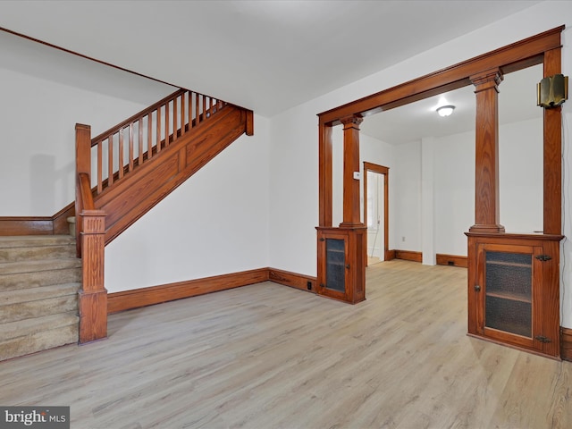 unfurnished living room featuring decorative columns, stairway, baseboards, and wood finished floors