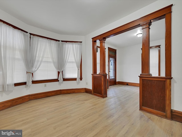 empty room with light wood-style flooring, decorative columns, and baseboards