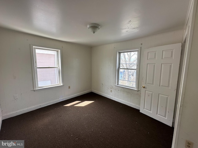 unfurnished bedroom featuring wooden walls, baseboards, and dark colored carpet
