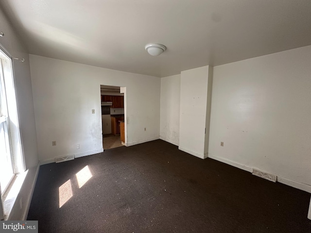 unfurnished room featuring visible vents, baseboards, and dark carpet
