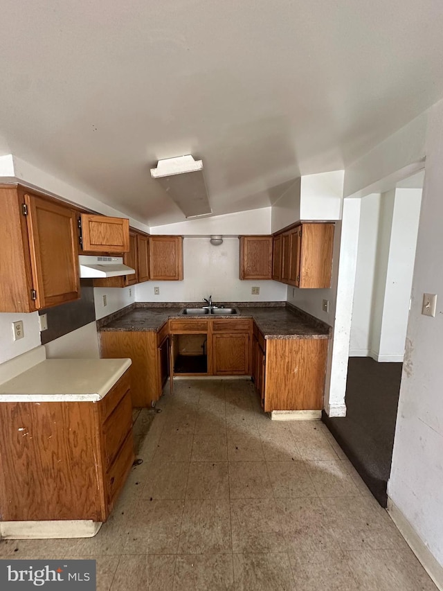 kitchen with a sink, brown cabinetry, baseboards, and under cabinet range hood