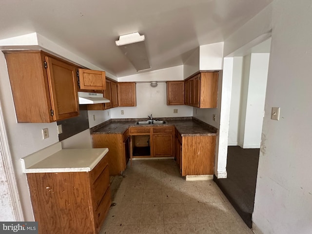 kitchen featuring a sink, brown cabinetry, lofted ceiling, and under cabinet range hood
