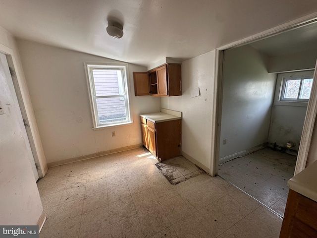 kitchen with light floors, brown cabinetry, vaulted ceiling, light countertops, and baseboards