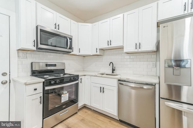 kitchen featuring white cabinets, a sink, decorative backsplash, light stone countertops, and appliances with stainless steel finishes