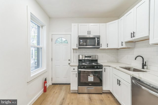 kitchen featuring decorative backsplash, stainless steel appliances, white cabinets, and a sink