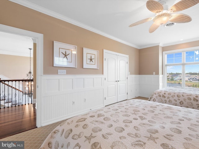 bedroom with a decorative wall, a closet, ornamental molding, carpet flooring, and wainscoting