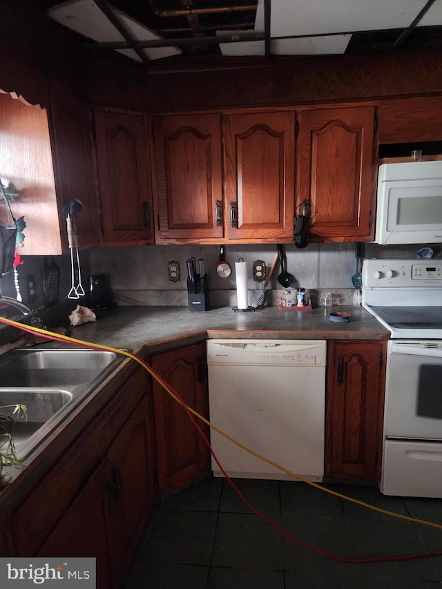 kitchen featuring a sink, brown cabinetry, dark tile patterned floors, and white appliances