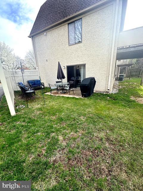 rear view of house featuring stucco siding, a yard, fence, a patio, and roof with shingles