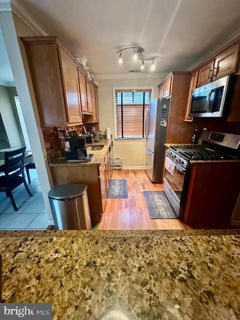 kitchen featuring light stone countertops, stainless steel appliances, ornamental molding, light wood finished floors, and a sink
