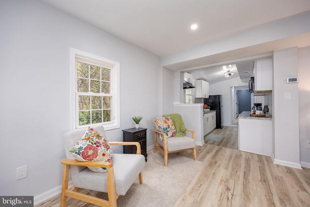 sitting room featuring light wood-style flooring, baseboards, and vaulted ceiling