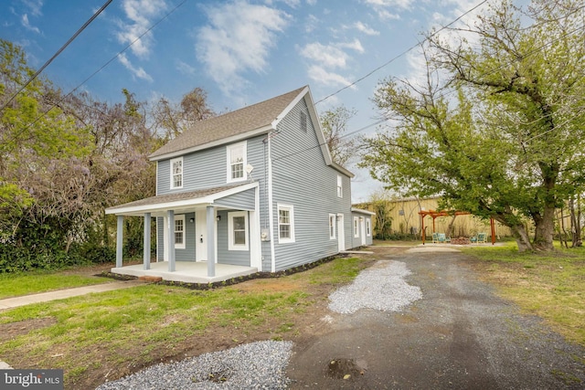 traditional home featuring a shingled roof, covered porch, and gravel driveway