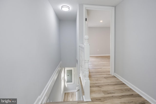 hall with wood finished floors and an upstairs landing