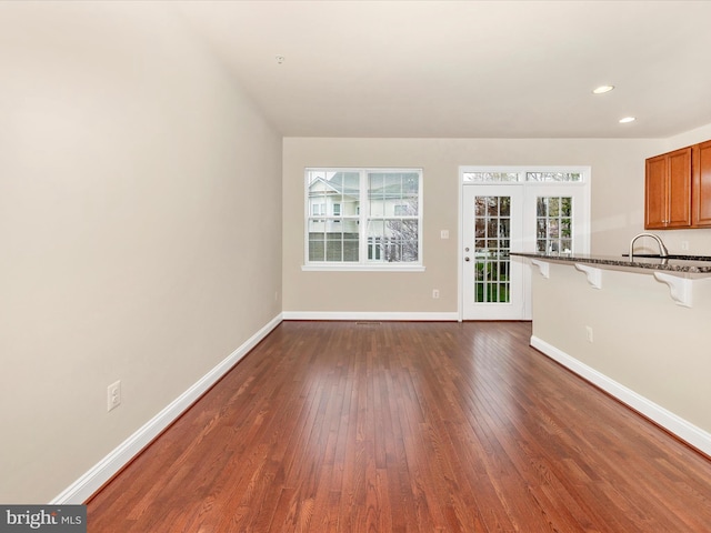 unfurnished living room featuring a healthy amount of sunlight, baseboards, and dark wood finished floors