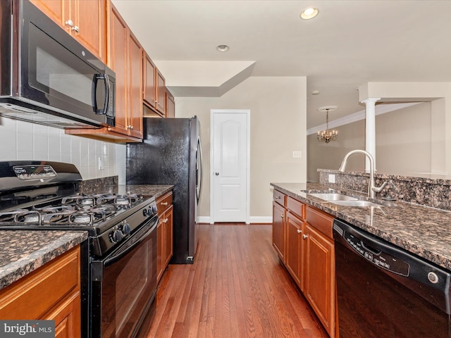 kitchen with a sink, brown cabinets, black appliances, dark wood-type flooring, and backsplash