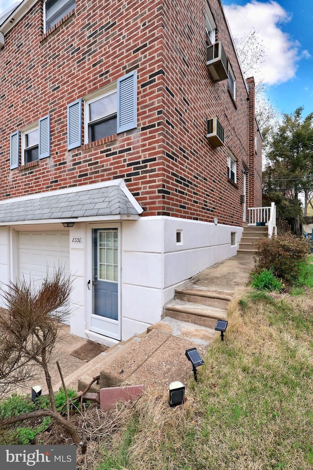 exterior space featuring an attached garage, an AC wall unit, and brick siding