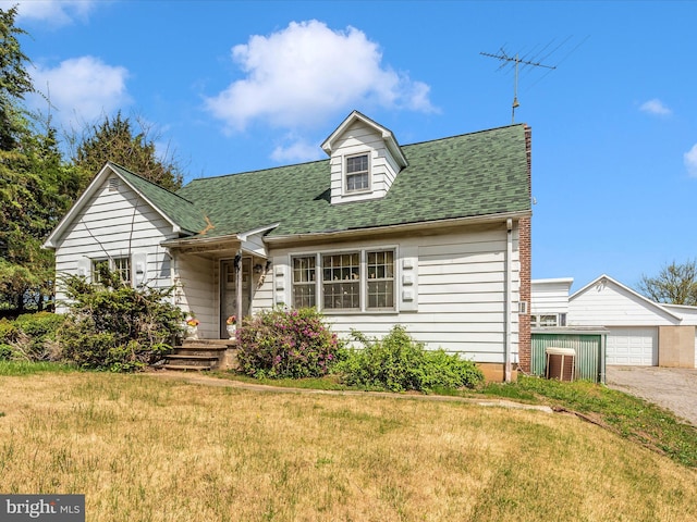 new england style home featuring a front lawn, roof with shingles, and an outdoor structure