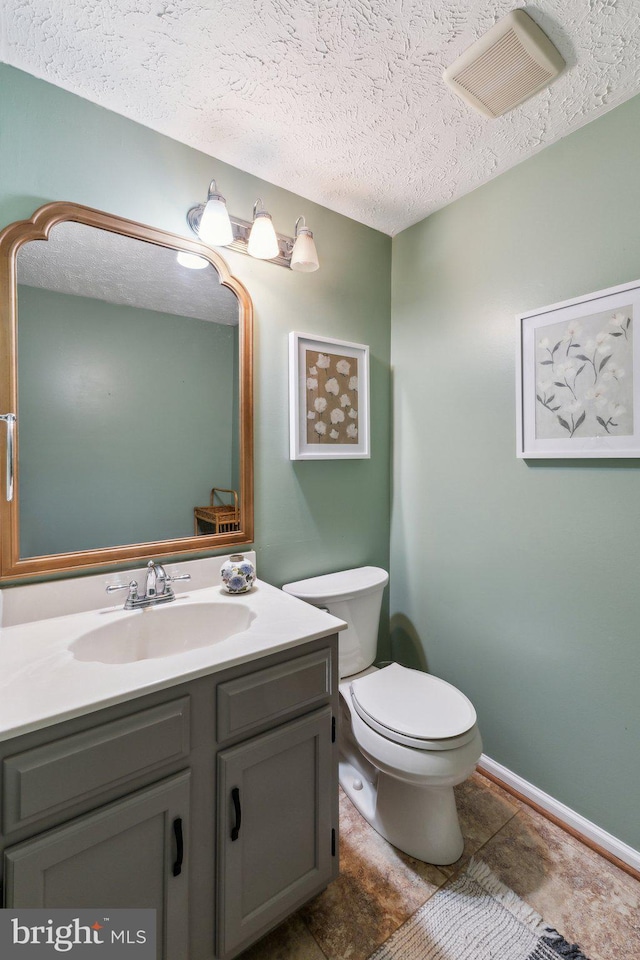 half bath featuring a textured ceiling, visible vents, vanity, baseboards, and toilet