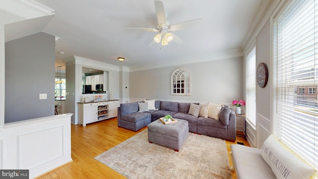 living room with a ceiling fan, ornamental molding, and light wood-style flooring