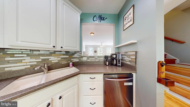 kitchen featuring stainless steel dishwasher, dark countertops, a sink, decorative backsplash, and white cabinetry