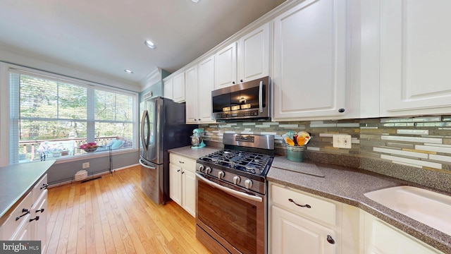 kitchen with white cabinets, decorative backsplash, stainless steel appliances, and light wood finished floors