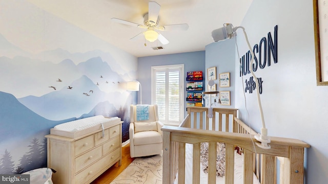 bedroom featuring ceiling fan, wood finished floors, visible vents, and a nursery area