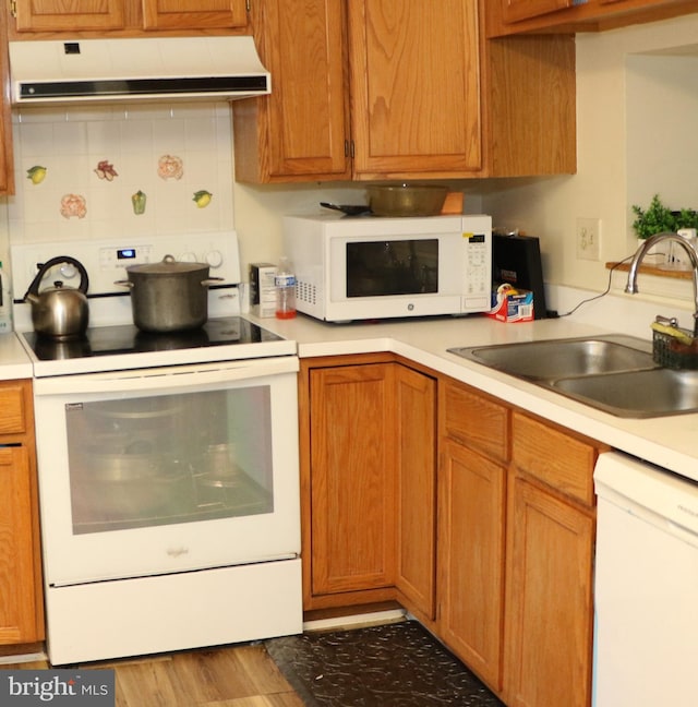 kitchen with white appliances, light countertops, backsplash, exhaust hood, and a sink