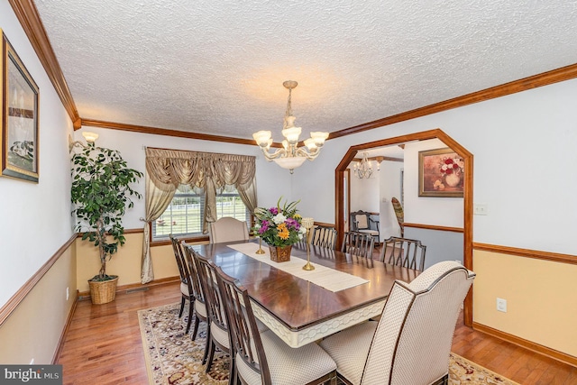 dining area with light wood finished floors, a notable chandelier, a textured ceiling, and ornamental molding