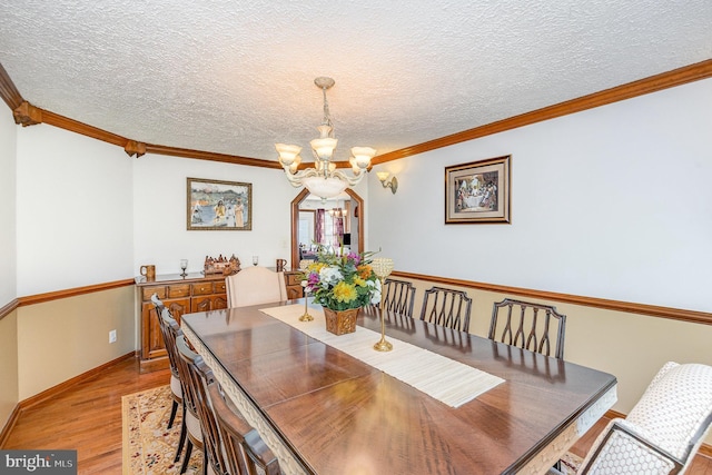 dining room with baseboards, ornamental molding, a chandelier, a textured ceiling, and light wood finished floors