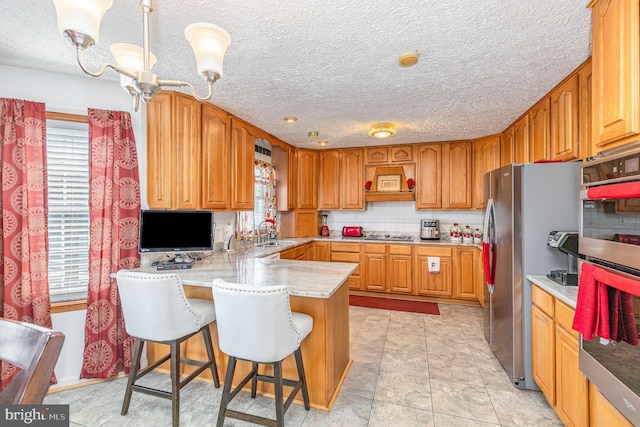 kitchen featuring a peninsula, a textured ceiling, a breakfast bar, appliances with stainless steel finishes, and a sink
