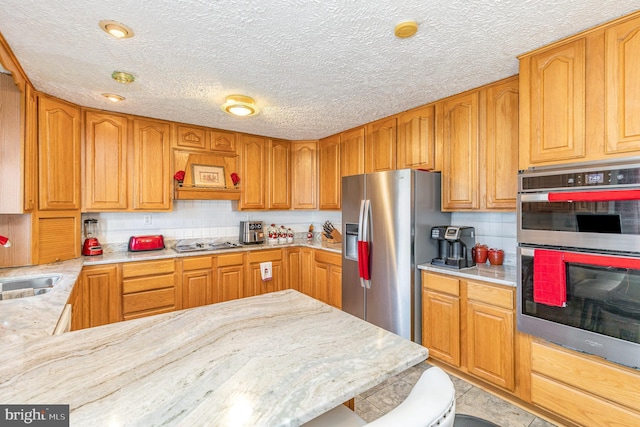 kitchen with a textured ceiling, backsplash, light stone countertops, and stainless steel appliances