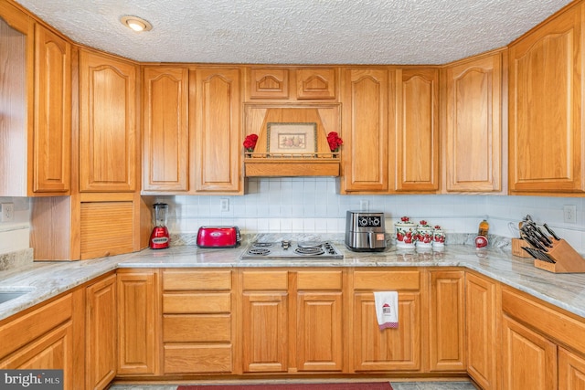 kitchen with brown cabinetry, a textured ceiling, and stainless steel stovetop