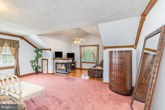 carpeted living area with ceiling fan, a multi sided fireplace, a textured ceiling, vaulted ceiling, and baseboards