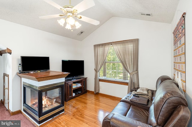 living room with visible vents, ceiling fan, light wood-type flooring, a textured ceiling, and vaulted ceiling
