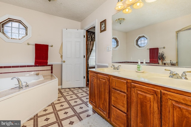 bathroom featuring a bath, a textured ceiling, double vanity, and a sink