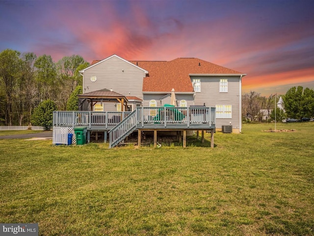 back of house at dusk with a deck, a gazebo, central AC unit, and a lawn