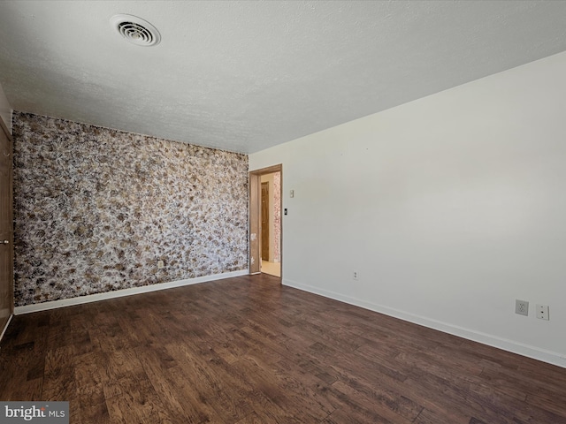unfurnished room with dark wood finished floors, baseboards, a textured ceiling, and visible vents