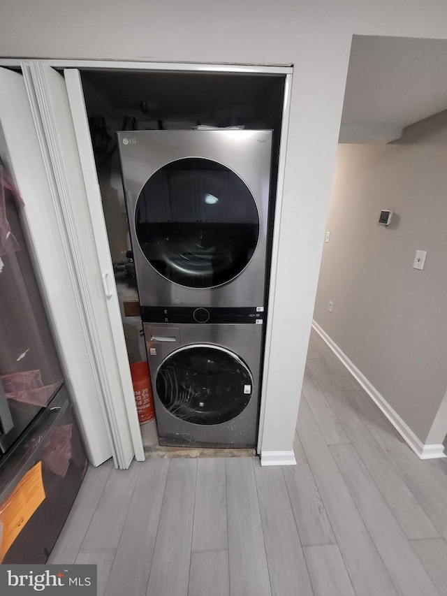 clothes washing area featuring laundry area, stacked washer and clothes dryer, wood finished floors, and baseboards