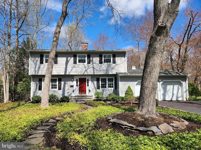 colonial inspired home featuring a chimney, aphalt driveway, and a garage