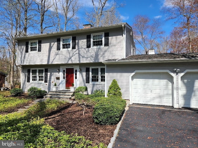 colonial inspired home with an attached garage, aphalt driveway, and a chimney
