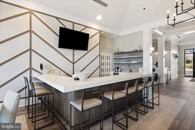 bar with visible vents, baseboards, wet bar, wood finished floors, and vaulted ceiling