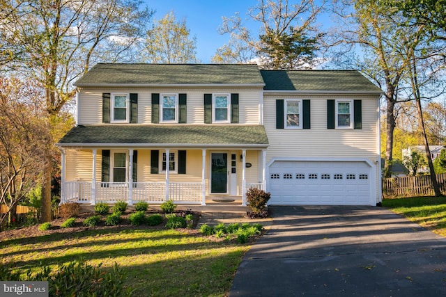 traditional-style home with a porch, fence, a garage, driveway, and a front lawn