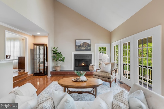 living area featuring recessed lighting, high vaulted ceiling, a lit fireplace, ornamental molding, and wood finished floors
