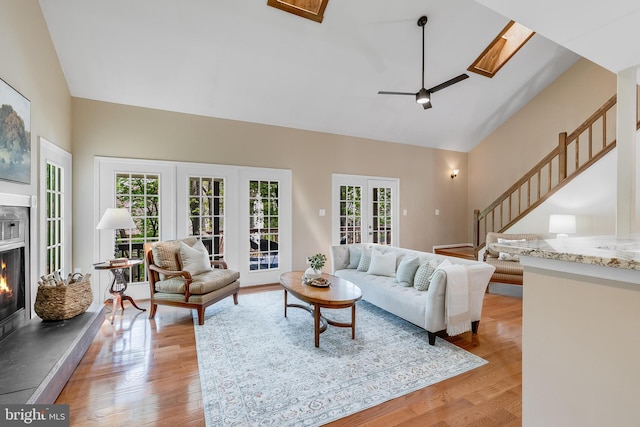 living room with a glass covered fireplace, a healthy amount of sunlight, high vaulted ceiling, and stairs