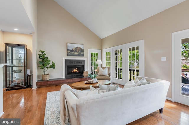 living room with baseboards, high vaulted ceiling, a lit fireplace, and light wood finished floors